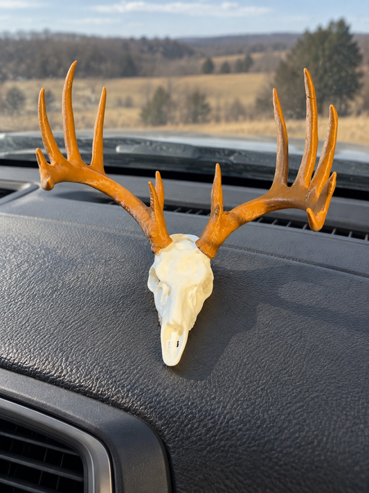 Ivory deer skull figure with brown antlers displayed on a truck dashboard in front of the windshield