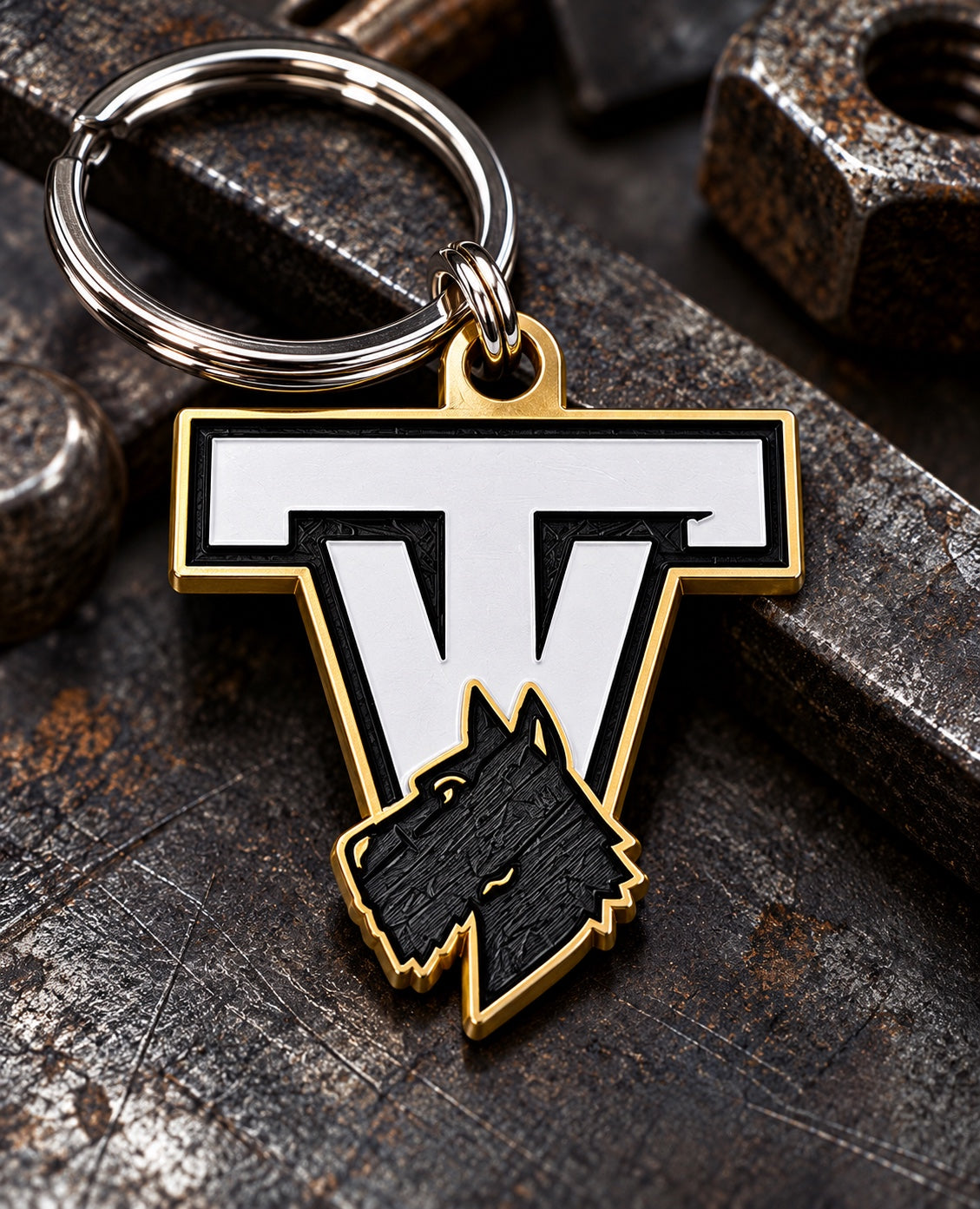 Tri-Valley Scotties TV keychain with black, white, and gold design and silver key ring on a dark industrial background
